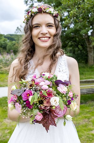 Billede af min bryllupsdag, hvor jeg står i hvid brudekjole med en buket blomster og en blomsterkrans i håret